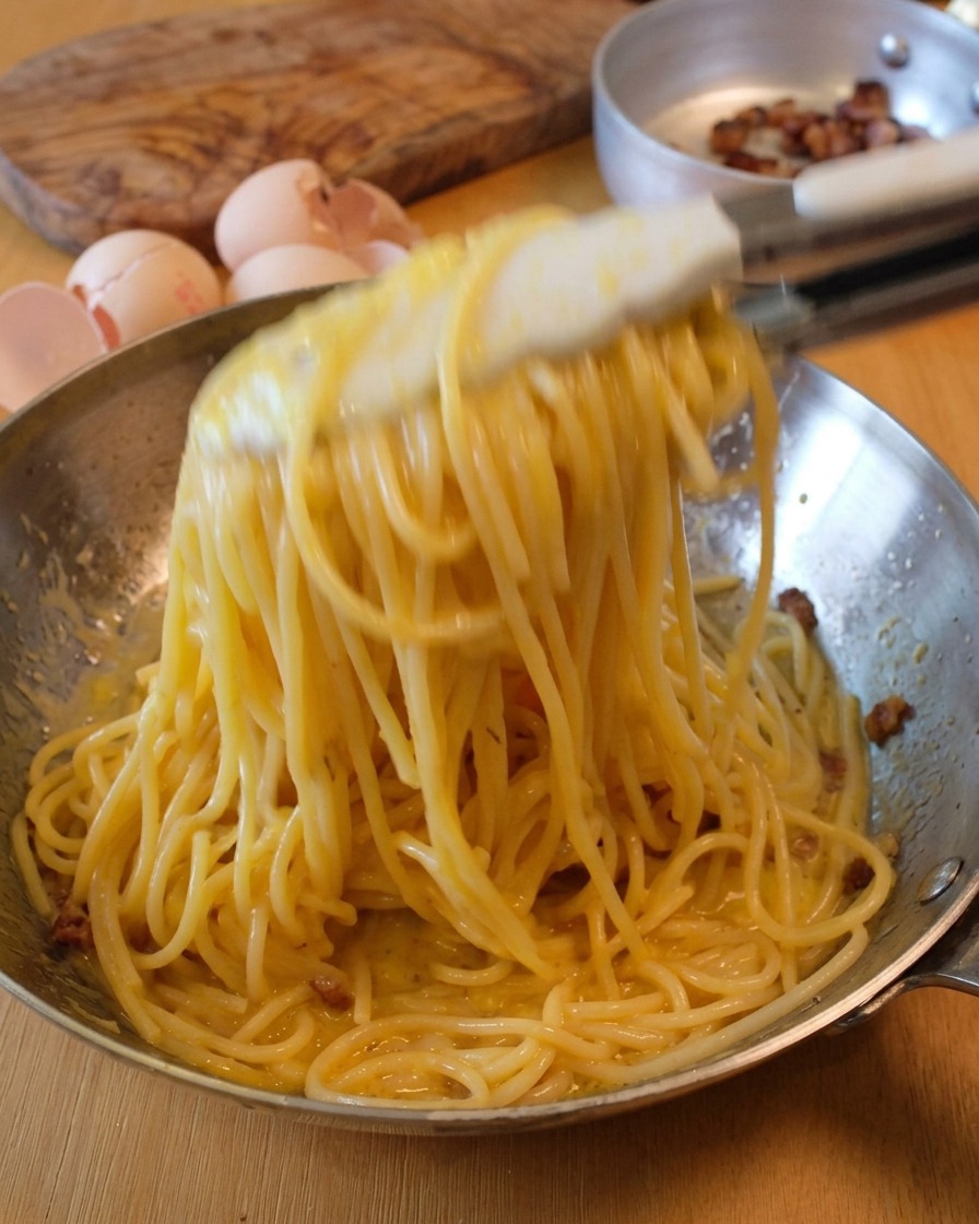 Spaghetti werden mit einer Zange in der Pfanne geschwenkt, bis die Sauce cremig ist.