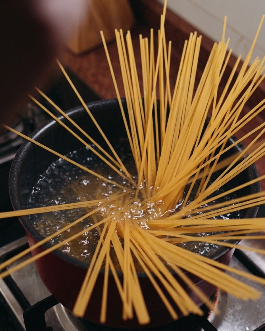 Trockene Spaghetti stehen senkrecht in einem Topf mit kochendem Wasser und fächern sich sternförmig aus.