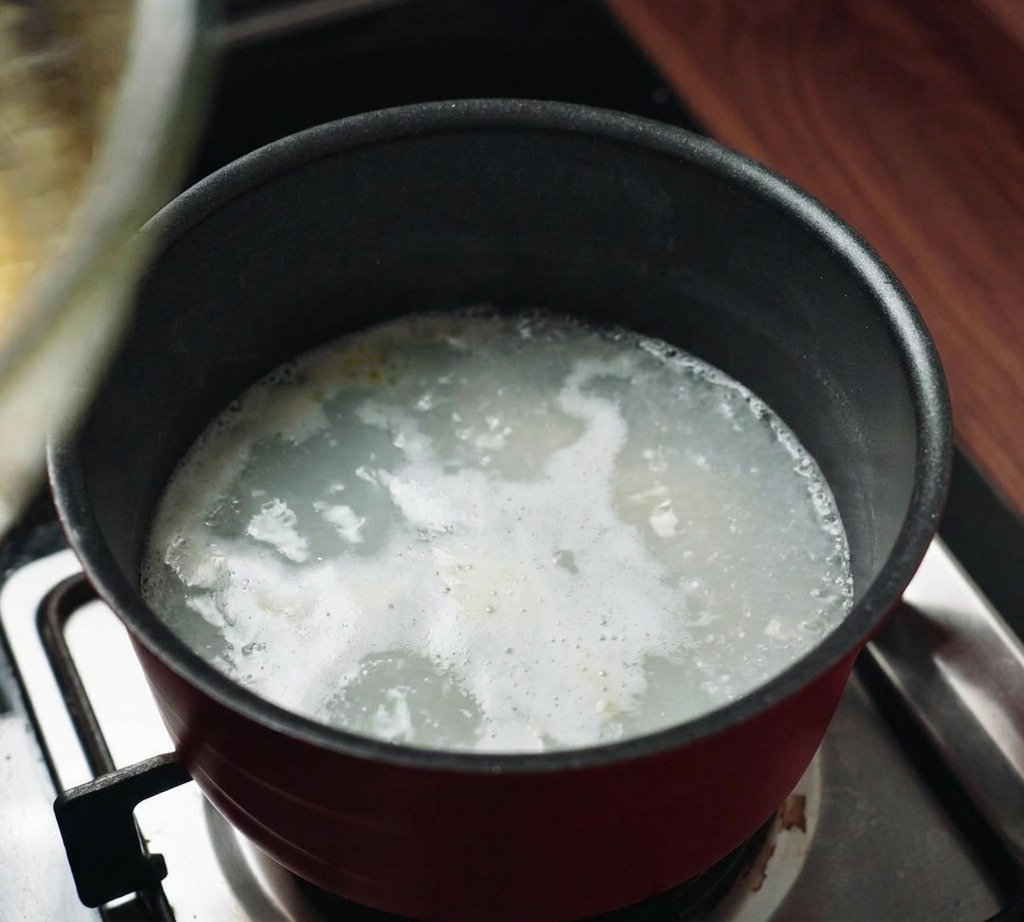Eine Glasschüssel wird auf einen Topf mit dampfendem Wasser auf dem Herd gesetzt, um ein Wasserbad zu erzeugen.