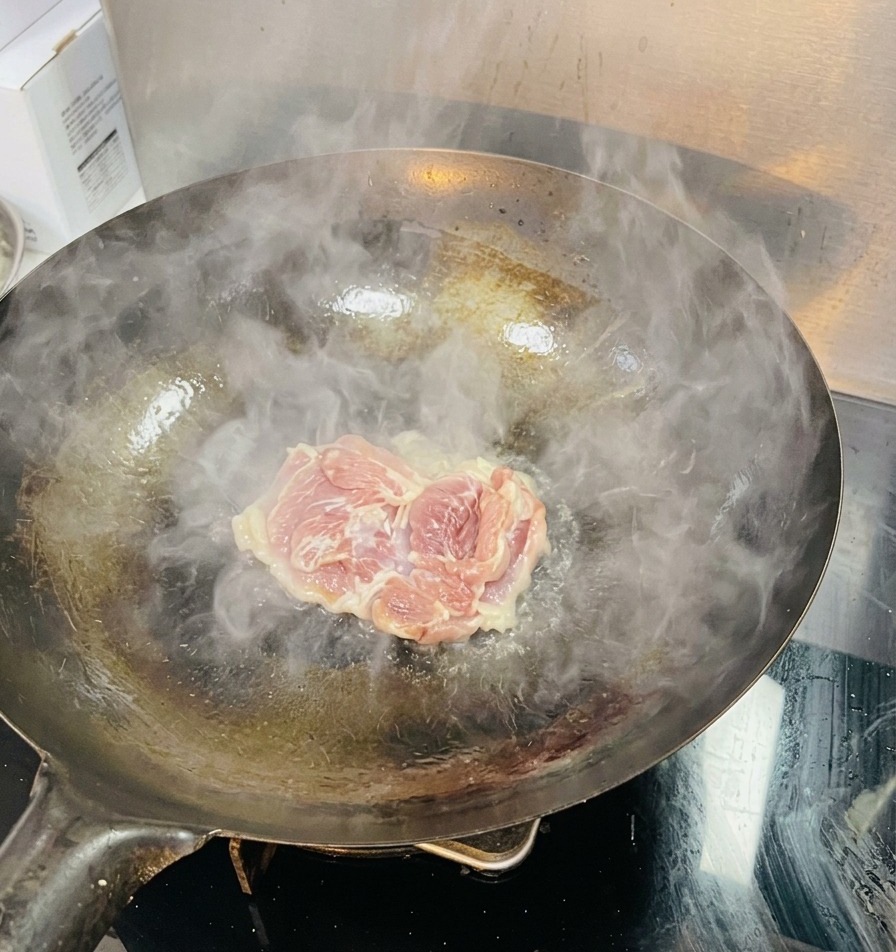 Eine rohe Hähnchenoberkeule wird in einen heißen Wok mit dampfendem und schimmerndem Öl gelegt.
