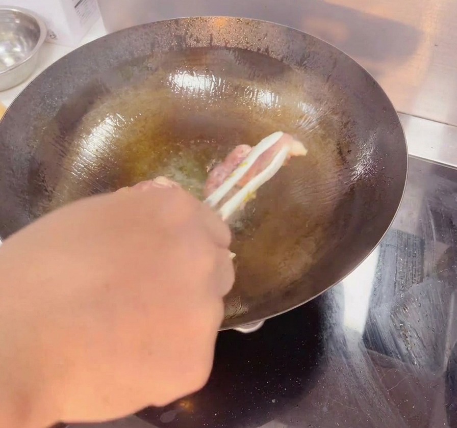 Eine Grillzange wendet eine Hähnchenoberkeule in einem dunklen Wok, um die knusprige, goldbraune Haut zu zeigen.