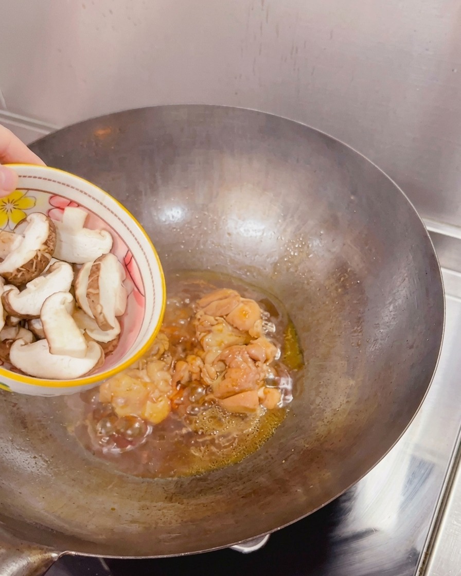 Frische, in Scheiben geschnittene Shiitake-Pilze werden aus einer Schüssel in einen Wok mit angebratenem Hähnchen und köchelnder Sauce gegeben.