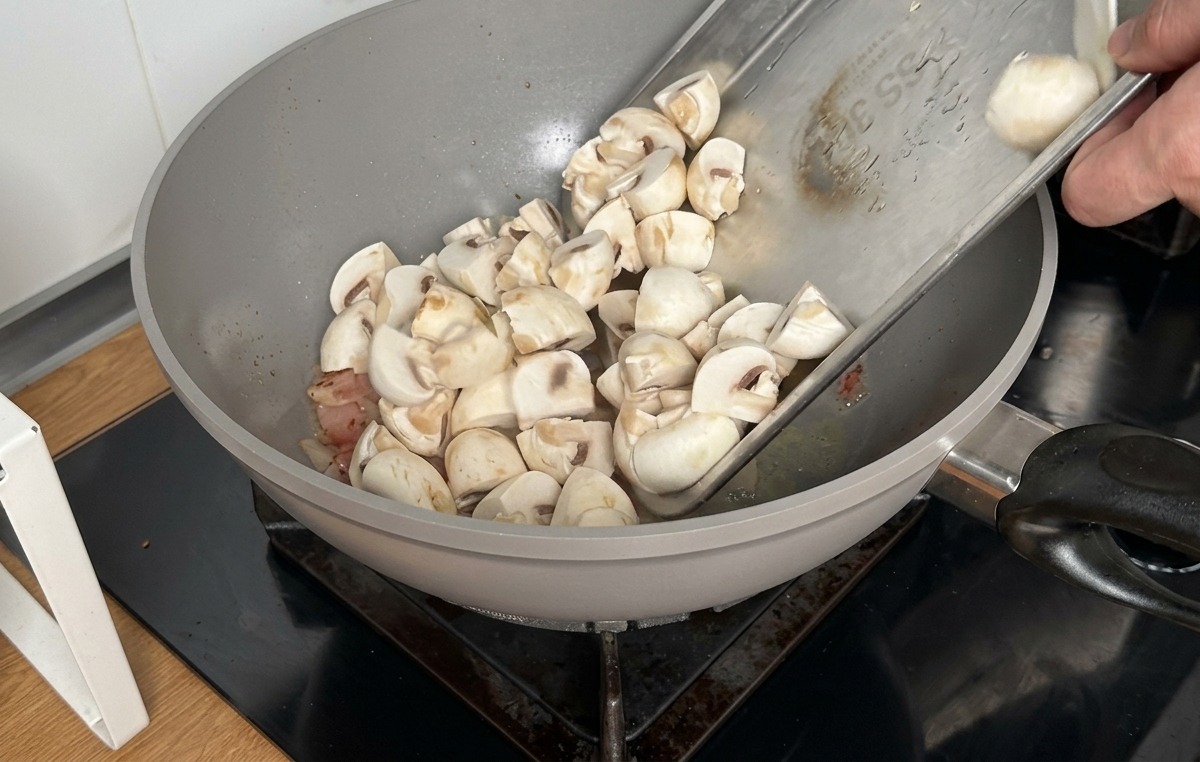 Geviertelte Champignons werden zum gebratenen Speck in den Wok gegeben.