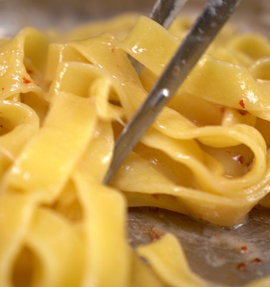 Tagliatelle werden mit Speck und köchelndem Nudelwasser in der Pfanne geschwenkt.