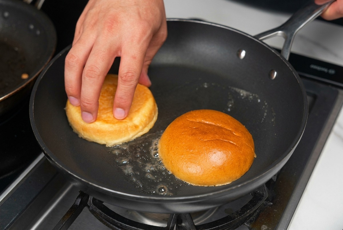 Halbierte Burgerbrötchen werden mit der Schnittseite nach unten in einer Pfanne mit schäumender Butter getoastet.