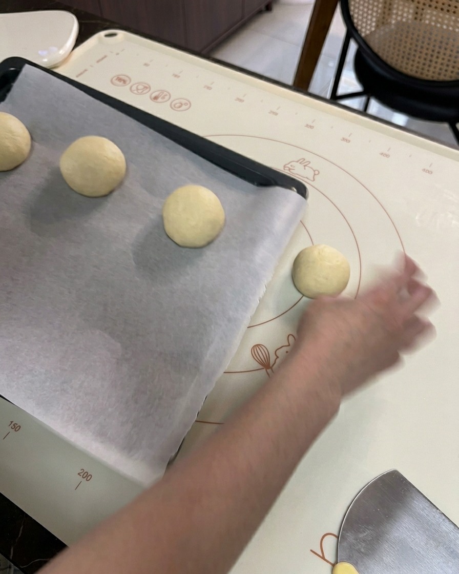 Eine Hand legt geformte, runde Teigkugeln auf ein schwarzes Backblech mit weißem Backpapier.