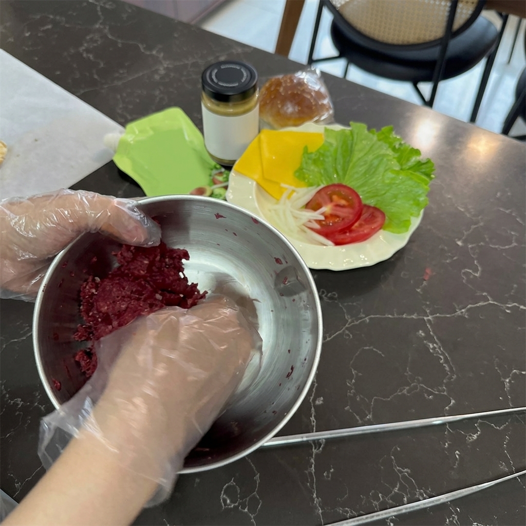 Hände in Plastikhandschuhen mischen rohes, hellrotes Rinderhackfleisch in einer Edelstahlschüssel.