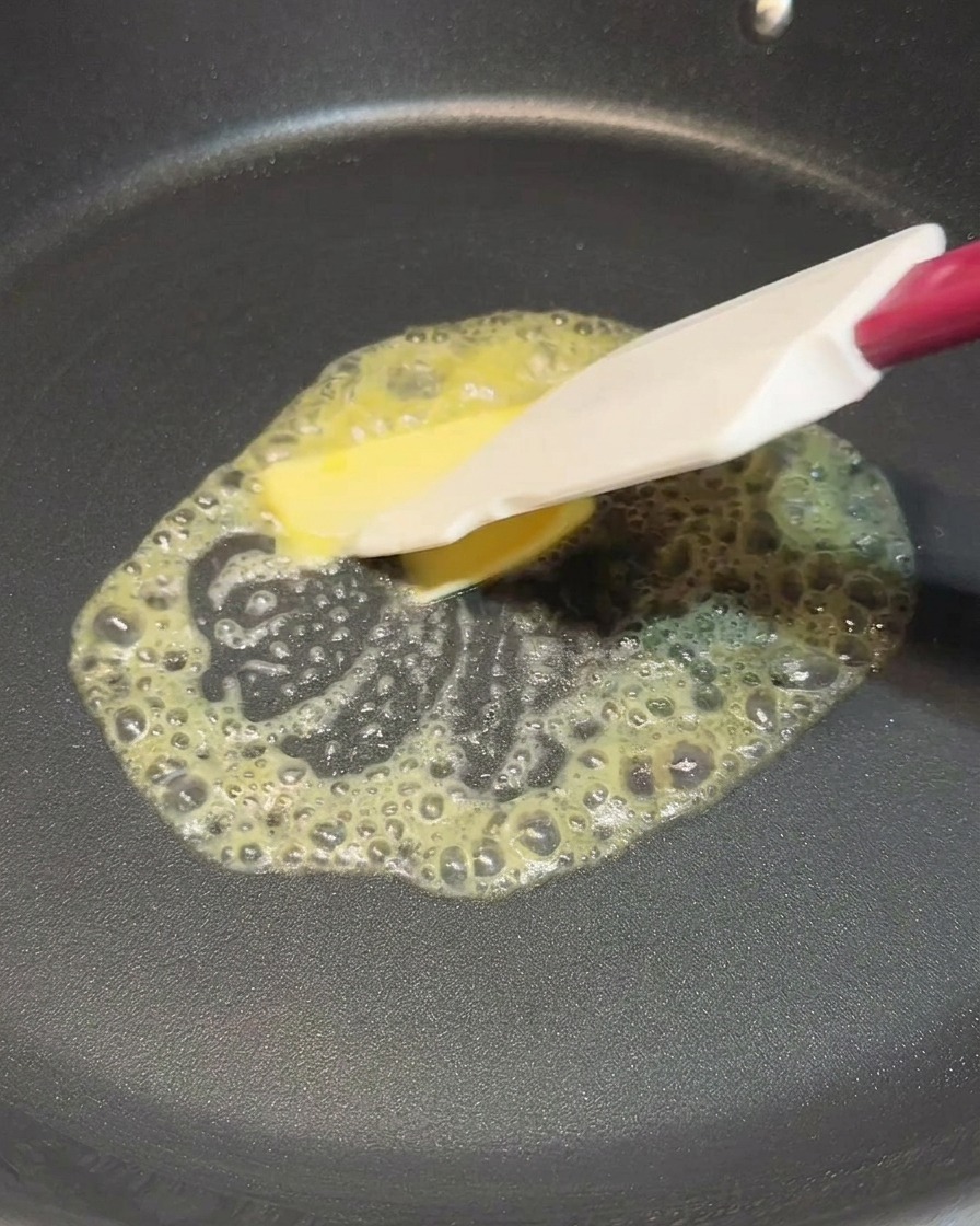 Ein Pfannenwender verteilt ein schmelzendes Stück Butter in einer heißen schwarzen Pfanne.