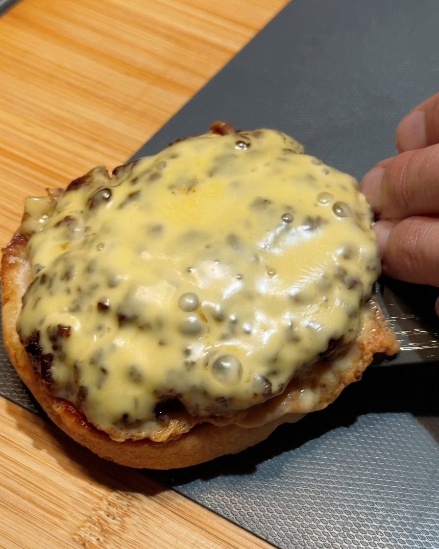 Ein Pfannenwender hebt zwei gestapelte Cheeseburger-Patties auf die untere Brötchenhälfte.