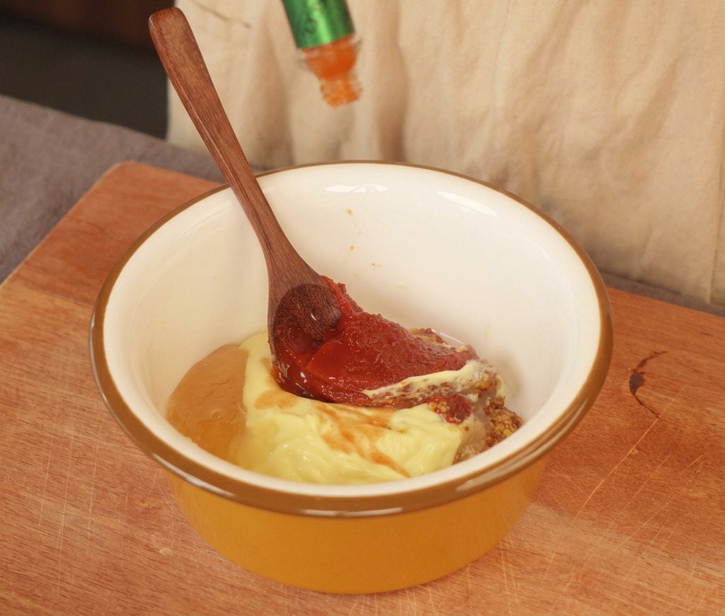 Scharfe Sauce wird in eine gelbe Schüssel mit Mayonnaise, grobkörnigem Senf und einer roten Paste gegeben.