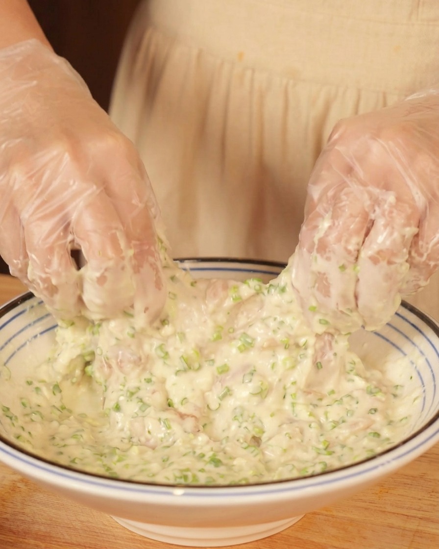 Behandschuhte Hände wenden ein Stück rohes Hähnchen in einer Schüssel mit dickem Teig.