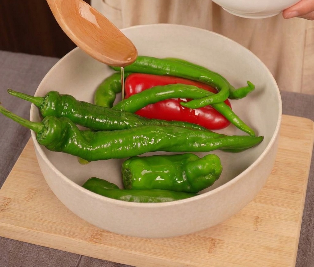 Klares Speiseöl wird von einem Holzlöffel über eine Mischung aus frischen roten und grünen Chilischoten in einer hellen Schüssel geträufelt.