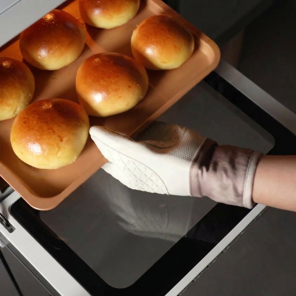 Ein Backblech mit frisch gebackenen, goldbraunen Buns wird aus dem Ofen gezogen.