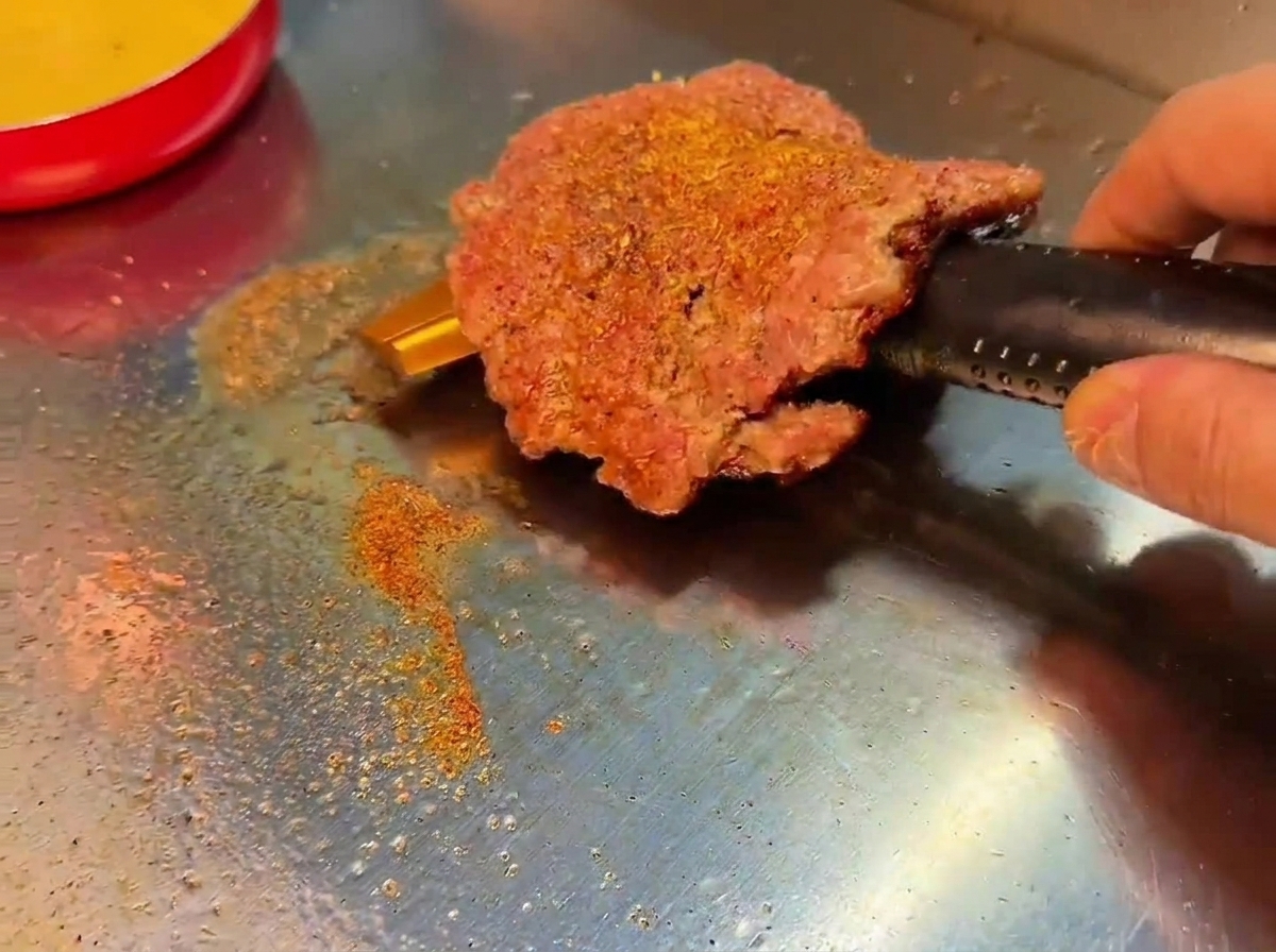 Ein Smashed Beef Patty wird auf dem Grill gewendet und zeigt eine dunkelbraune Kruste.