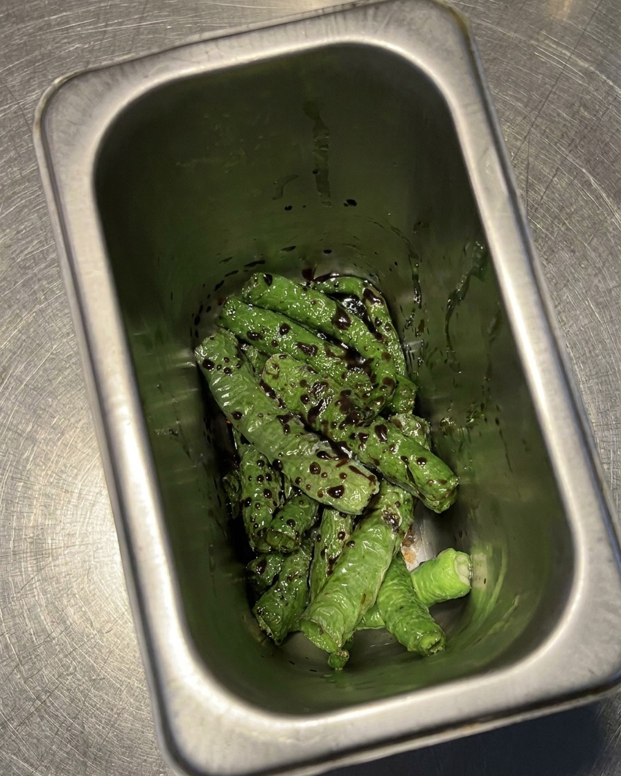 Frittierte grüne Chilis liegen in einem Behälter und sind mit einer dunklen Mischung aus Essig und Sojasauce bedeckt.