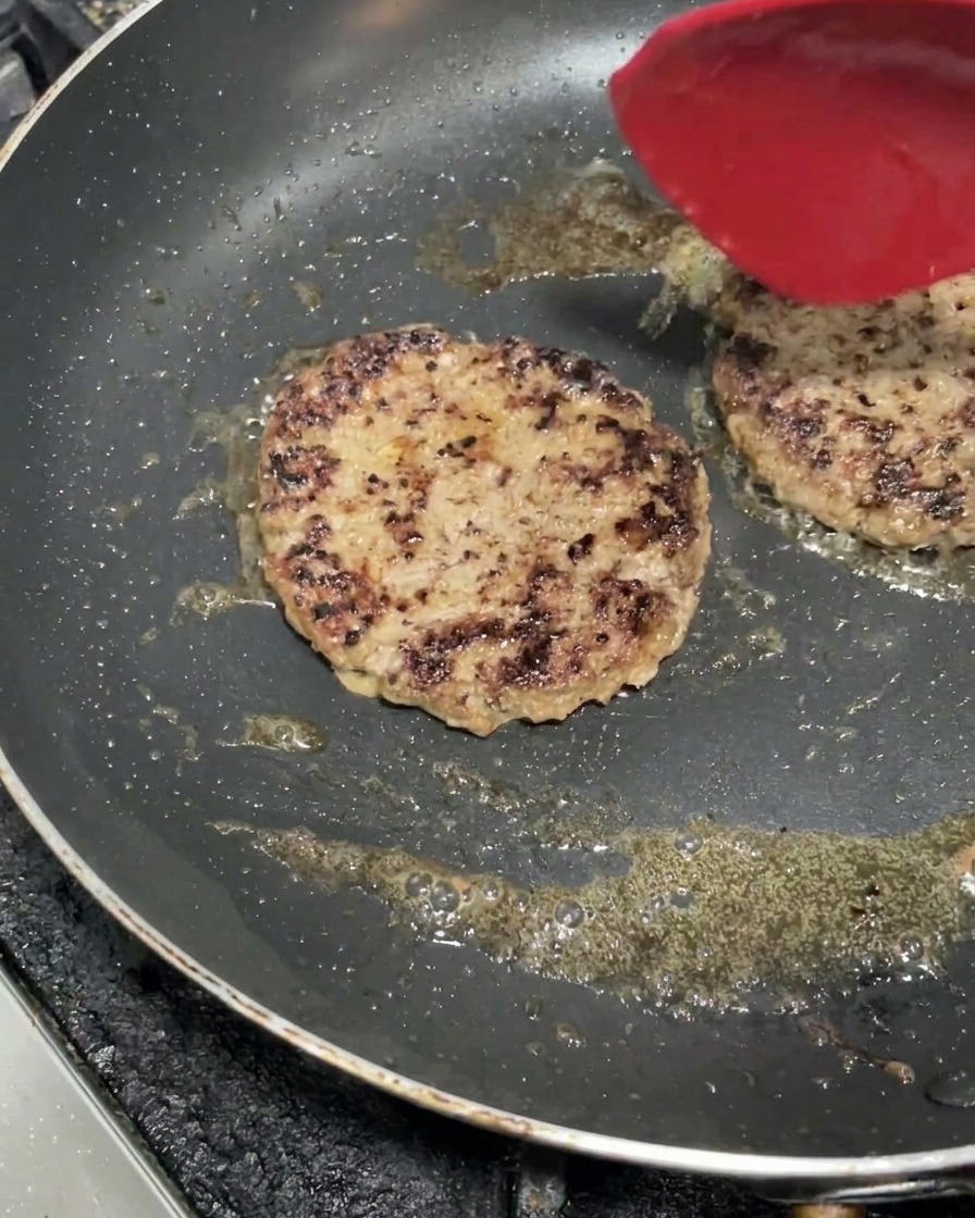 Zwei dicke Rinderpatties brutzeln in einer heißen Pfanne und bilden eine braune Kruste.