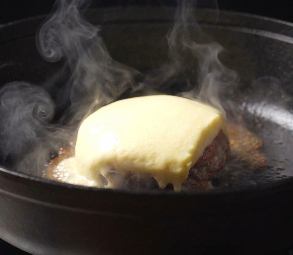 Eine Scheibe Käse schmilzt über einem Patty mit Tomatensauce in einer gusseisernen Pfanne.