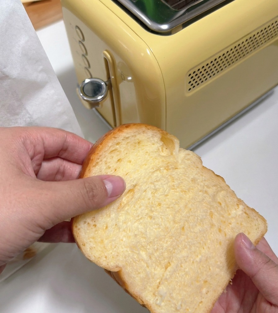 Eine Person schiebt eine dicke Scheibe Weißbrot in einen gelben Toaster im Retro-Stil.