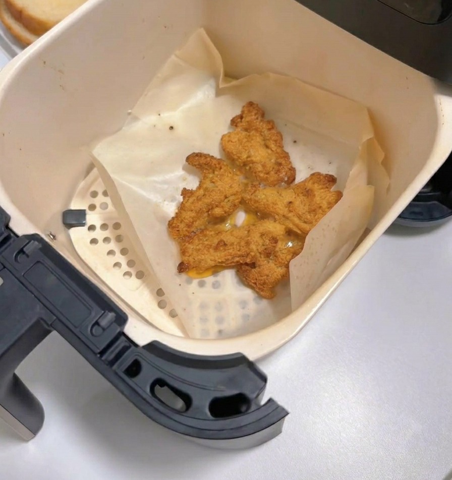 Ein herausgezogenes Airfryer-Fach zeigt mehrere Stücke fertig gegartes, goldbraunes Fried Chicken auf Backpapier.