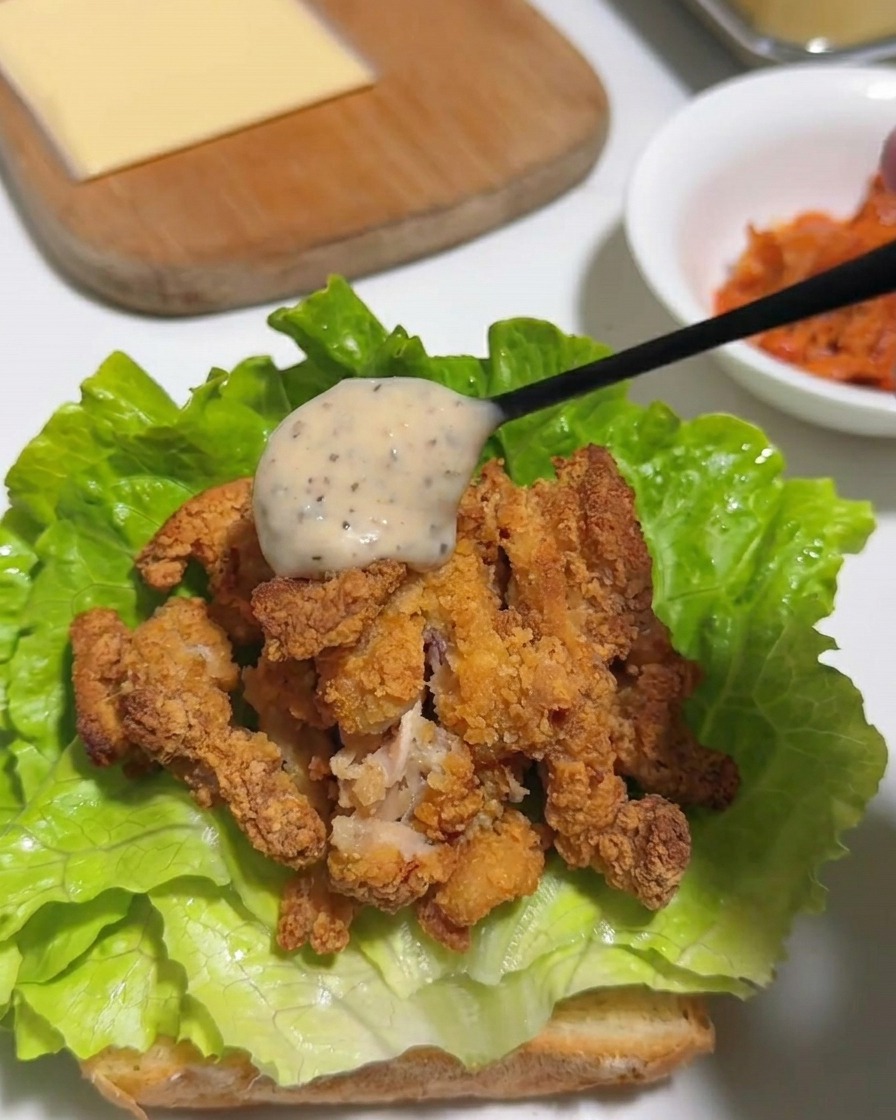 Ein Löffel mit cremiger, gesprenkelter Yuzu-Pfeffer-Mayonnaise wird über knuspriges Fried Chicken auf Salat gegossen.