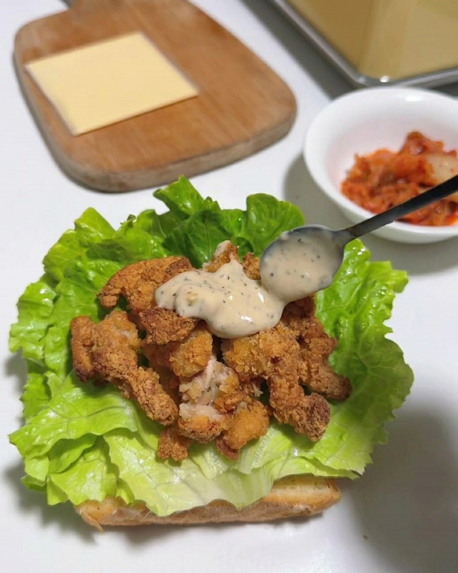 Eine quadratische Scheibe gelber Käse liegt auf den Hähnchenstreifen und dem Salat.