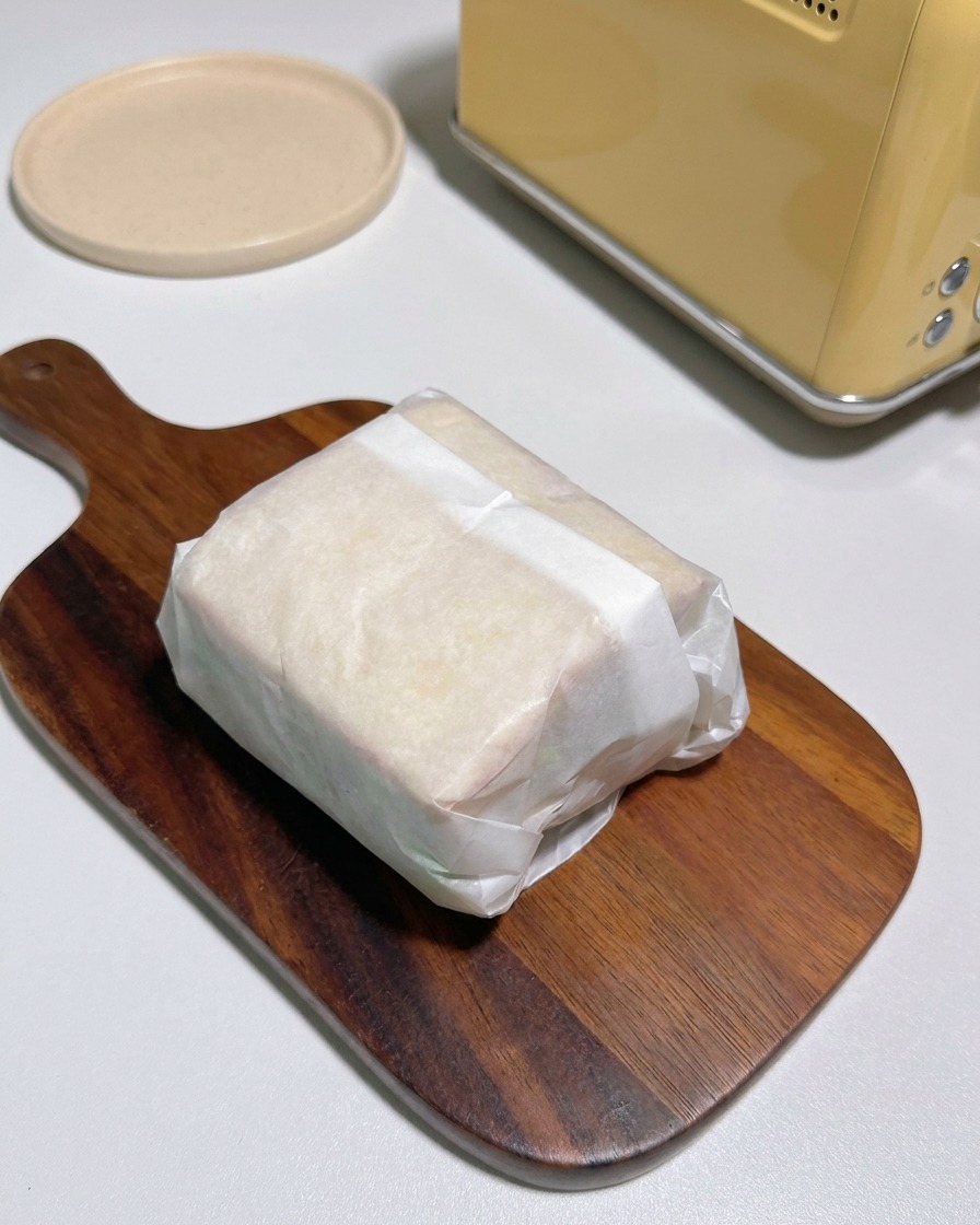 Zwei Hälften eines in Pergamentpapier eingewickelten Sandwiches zeigen Schichten von Toast, Hähnchen, Käse und Kimchi.