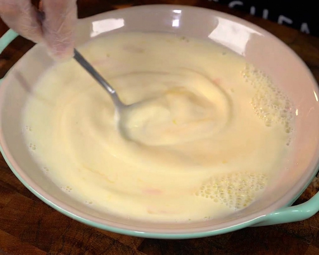 Ein Löffel rührt eine gelbe Ei-Milch-Mischung in einer Schüssel um.