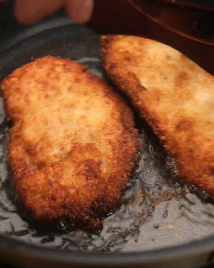 Ein knuspriges Stück Hähnchen wird mit einem Pfannenwender aus dem Öl gehoben.
