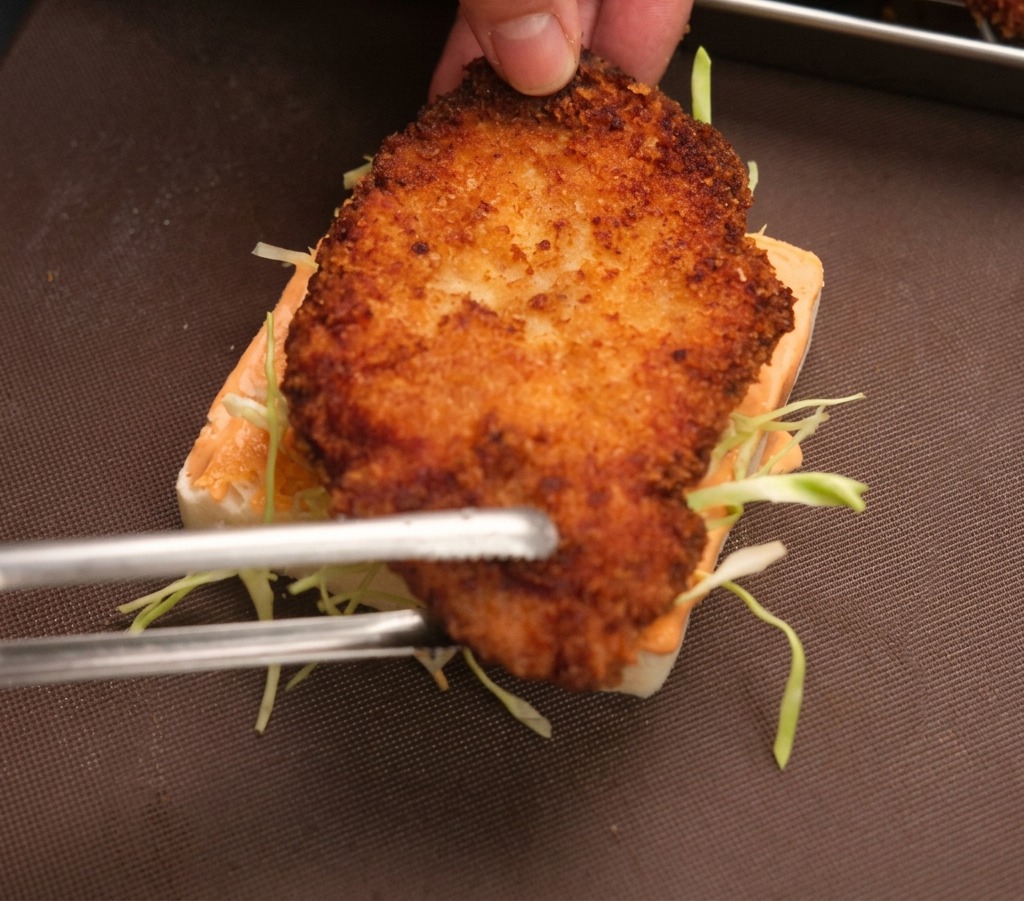 Ein knuspriges Hähnchenschnitzel wird auf das vorbereitete Brot mit Kohl und Sauce gelegt.