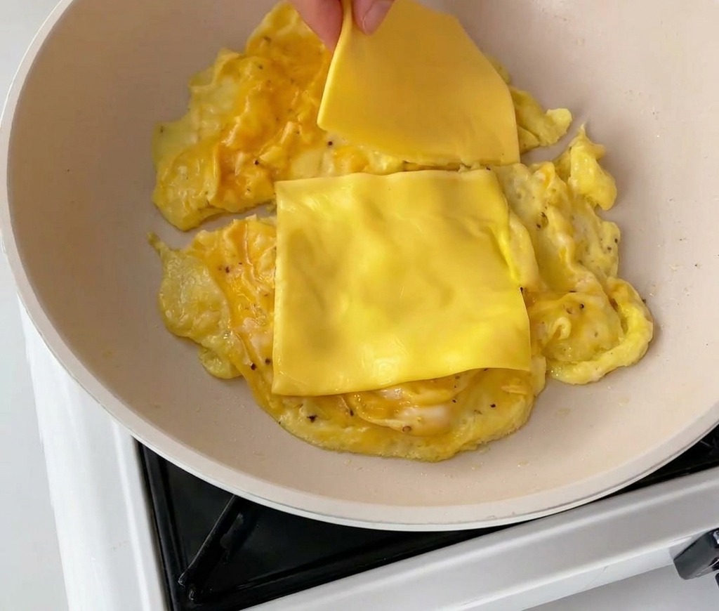 Cheddar-Käsescheiben werden auf das Rührei in der Pfanne gelegt.