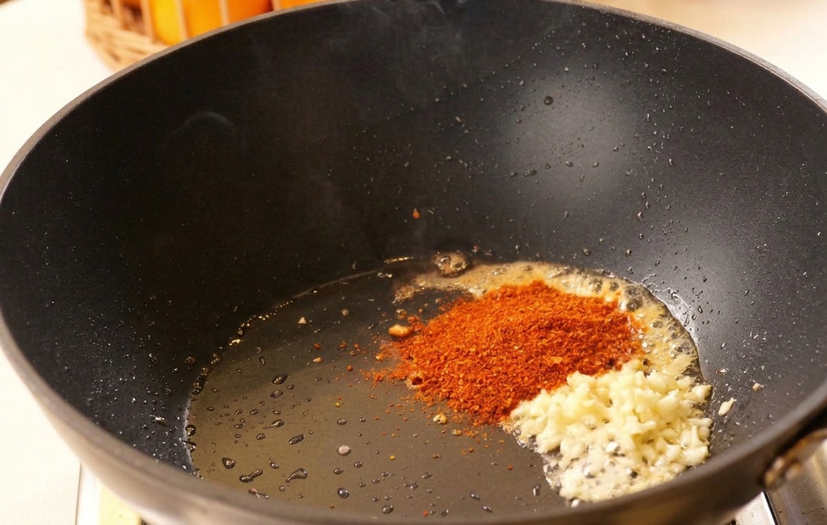 Gehackter Knoblauch und rotes Chilipulver in heißem Öl in einem schwarzen Wok.