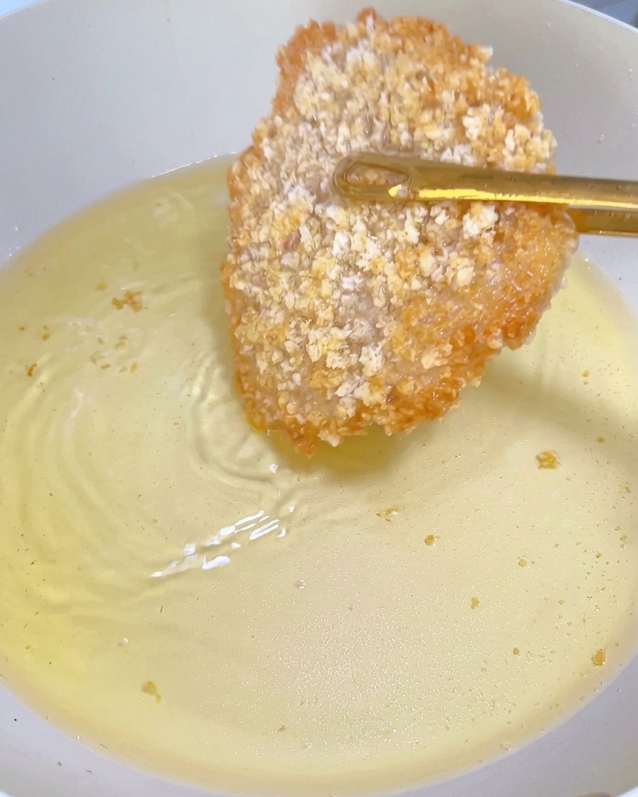 Ein teilweise frittiertes Hähnchenschnitzel mit goldbrauner Kruste wird mit einer Zange in der Pfanne gewendet.