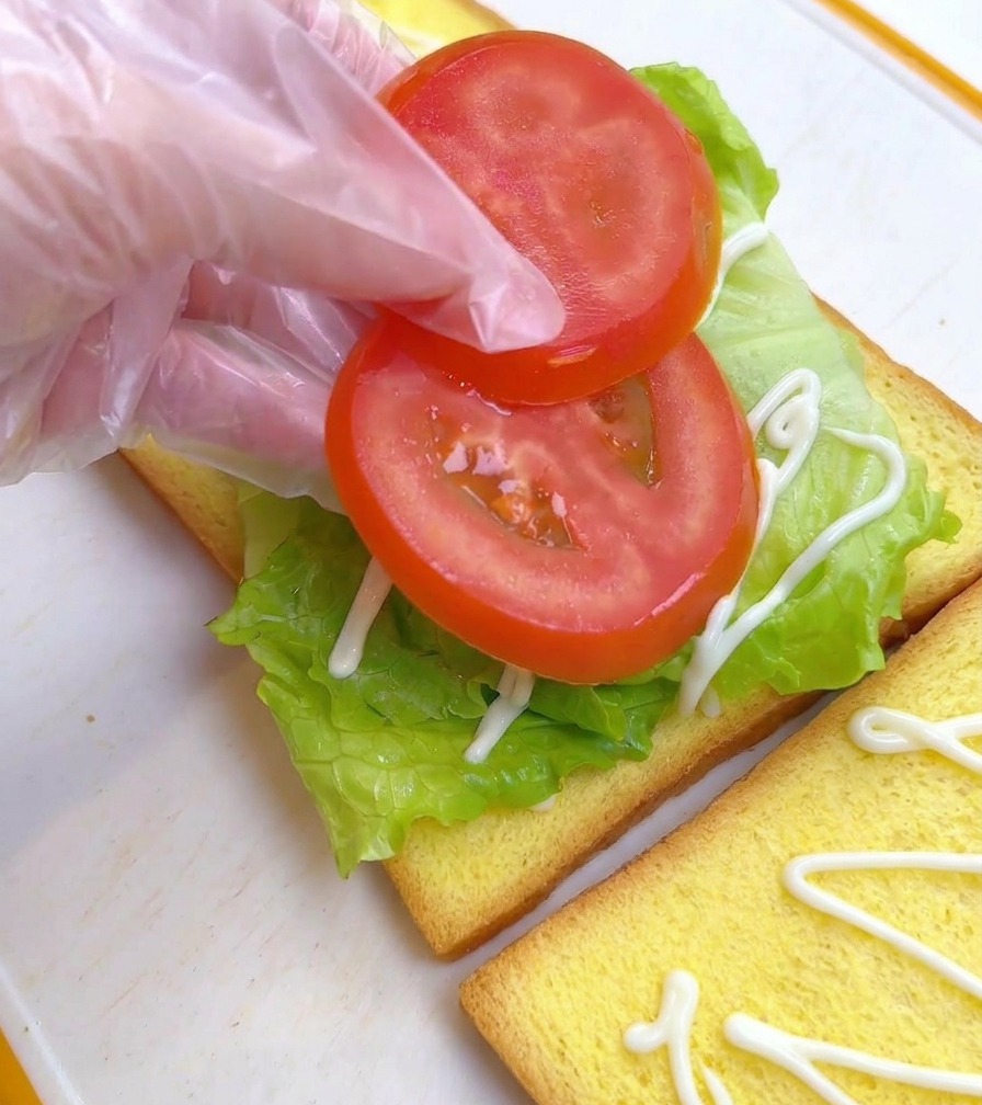 Finger legen zwei runde, rote Tomatenscheiben auf ein Salatblatt auf einer Toastscheibe.