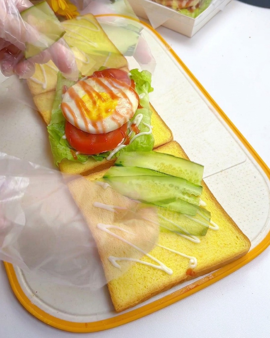 Hände ordnen dünne, diagonale Gurkenscheiben auf der zweiten Toastscheibe an.