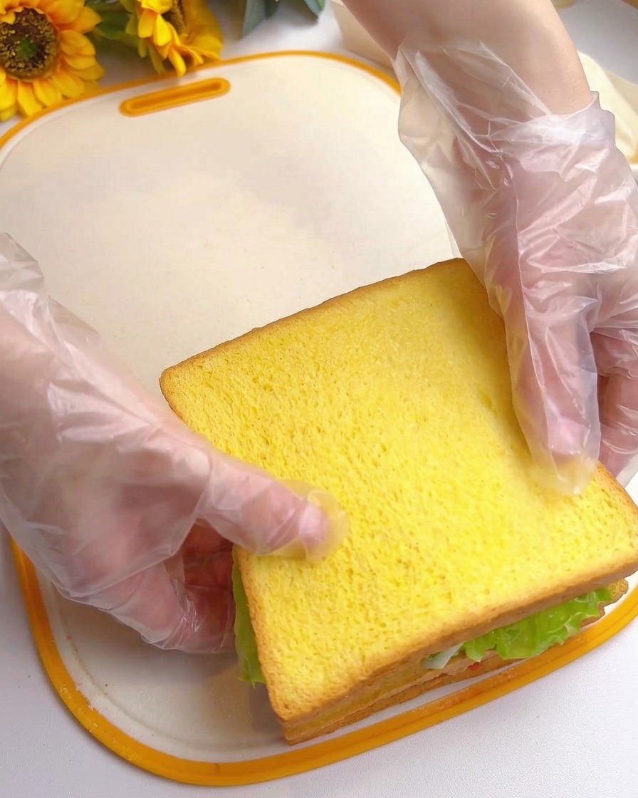 Zwei Hände drücken auf die oberste Toastscheibe, um ein hohes, mehrschichtiges Sandwich fertigzustellen.