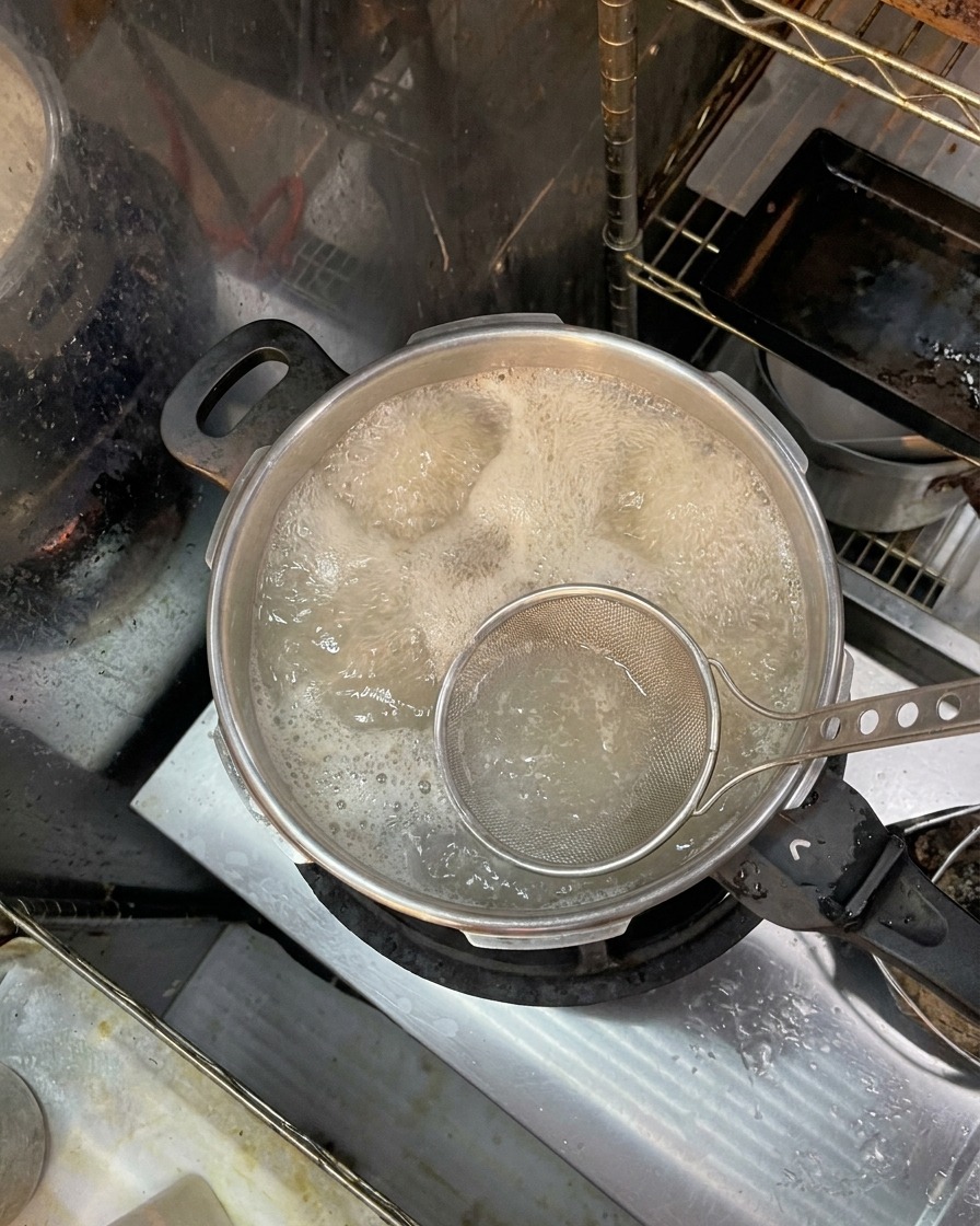 Ein Schaumlöffel entfernt bräunlichen Schaum und Unreinheiten von der Oberfläche des kochenden Wassers mit Knochen.