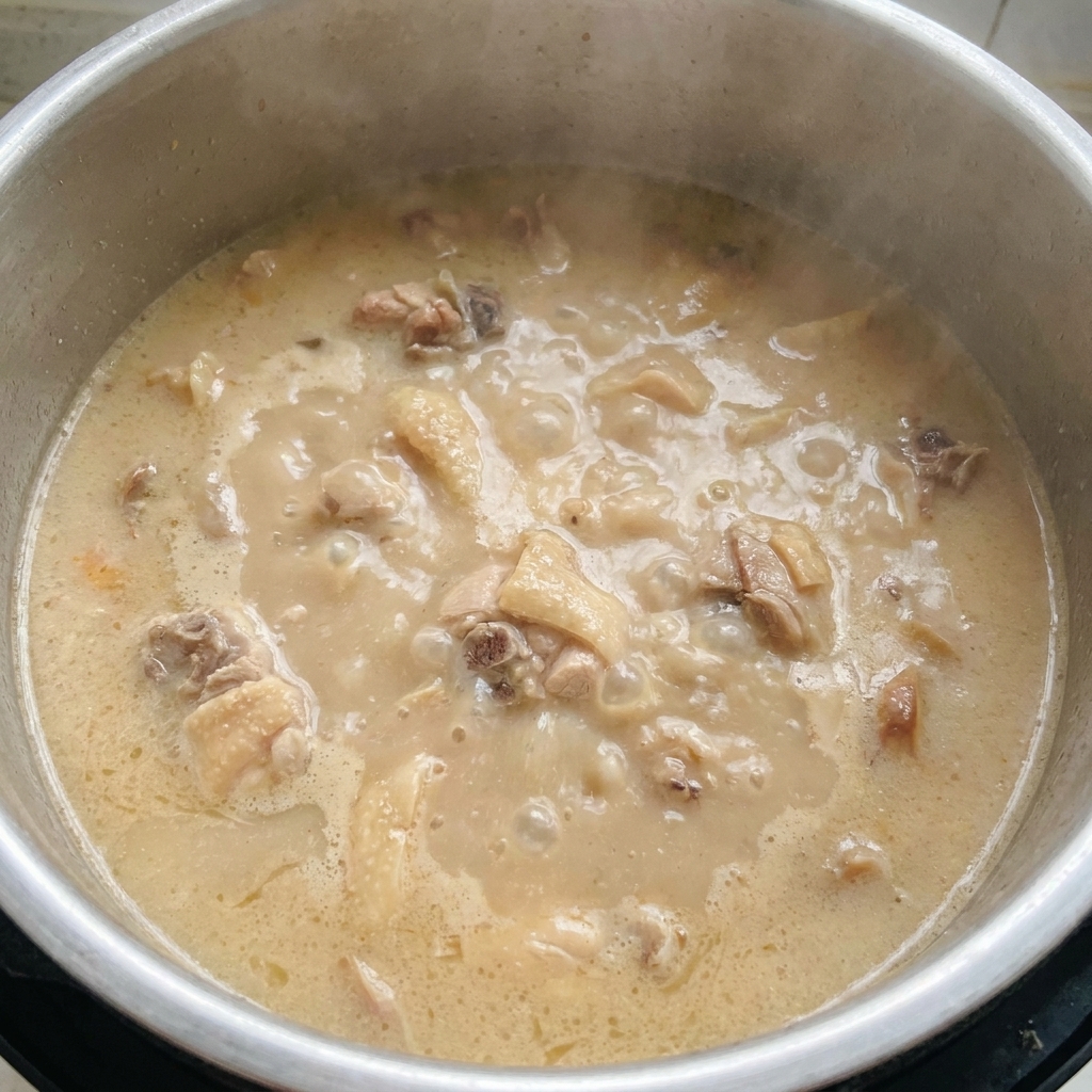 Ein Topf mit stark kochender, dicker und milchig-weißer Tonkotsu-Brühe, in der Fleischstücke sichtbar sind.