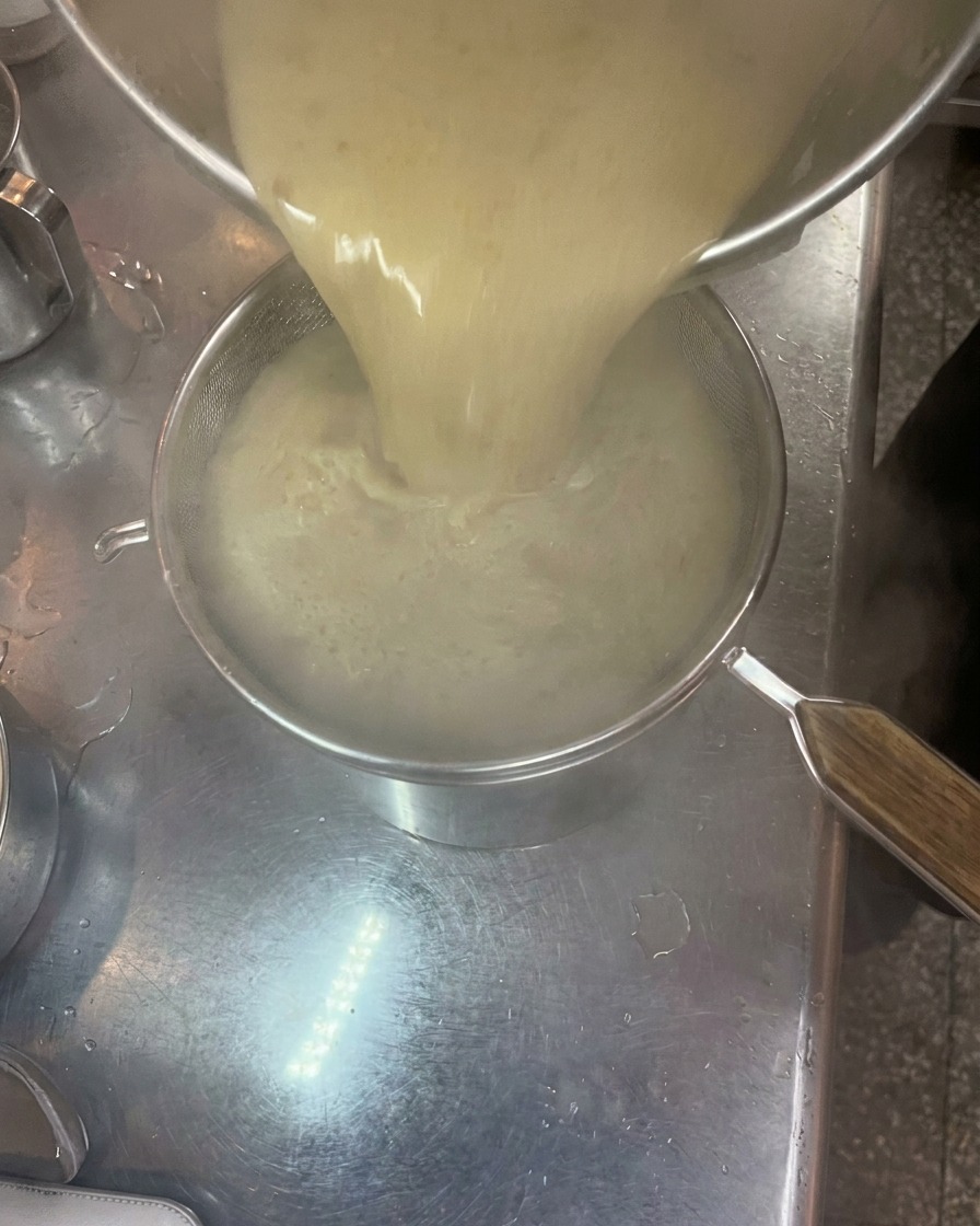 Dicke, cremige Tonkotsu-Brühe wird durch ein feines Sieb aus einem Topf in einen anderen gegossen.