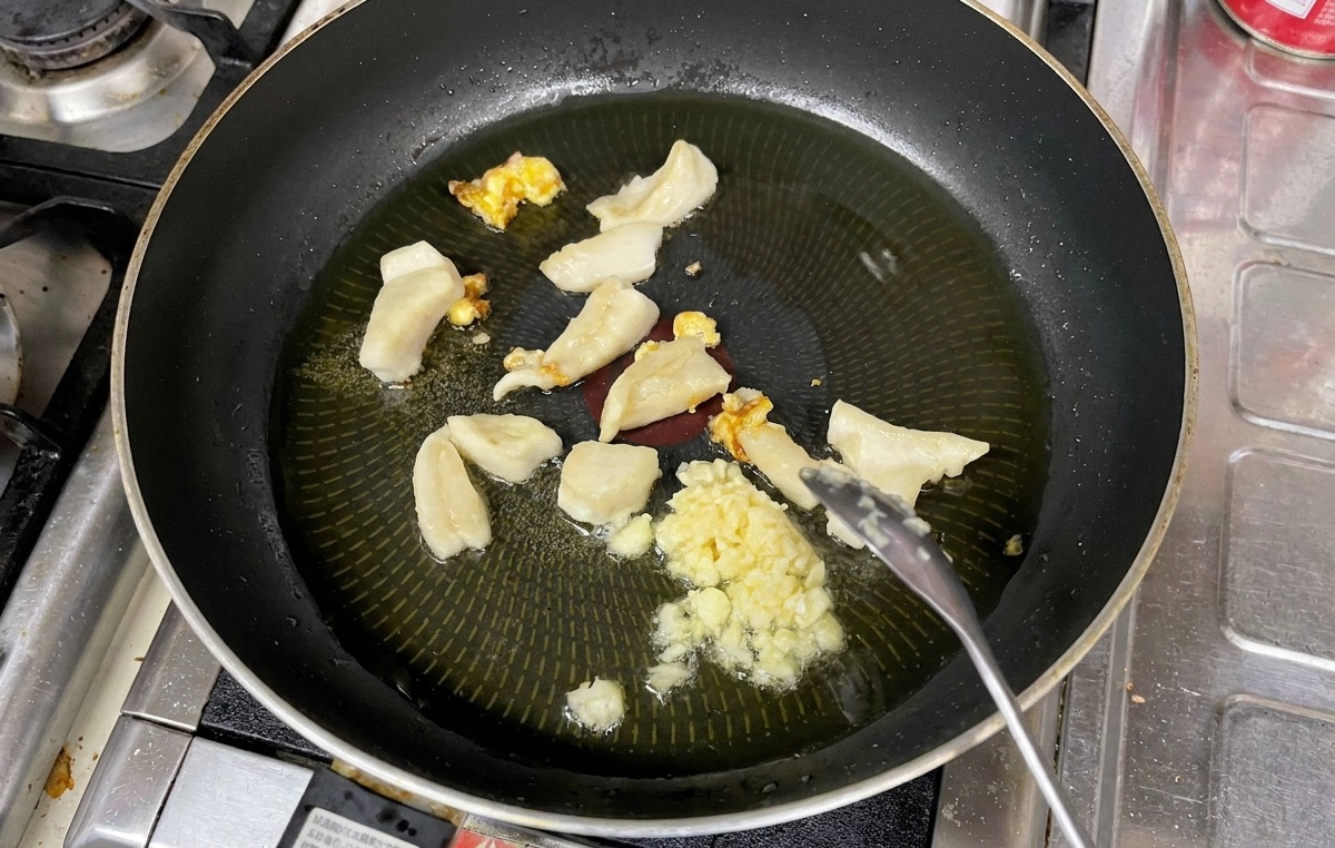 Gehackter Knoblauch wird mit einem Löffel zusammen mit Fettstücken in einer Pfanne mit heißem Öl umgerührt.