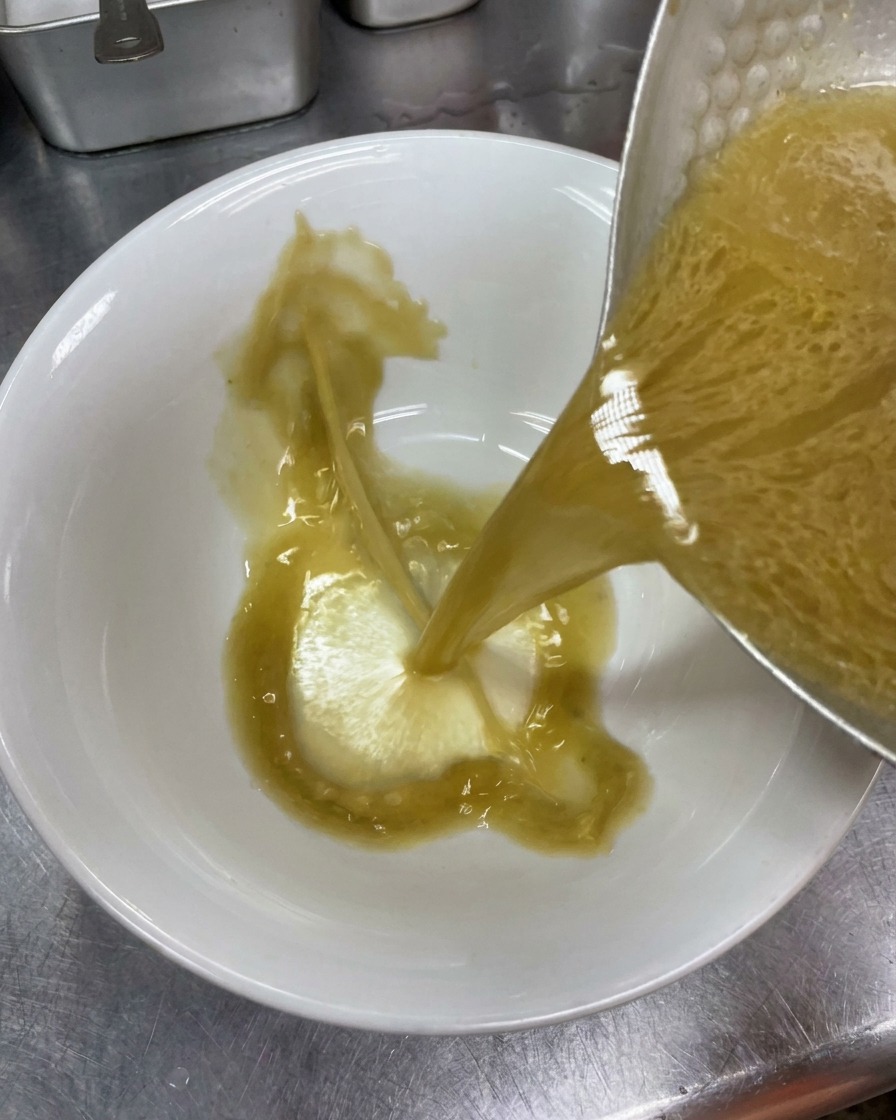 Heiße, opake Tonkotsu-Brühe wird aus einem Topf in eine saubere, weiße Keramikschüssel gegossen.
