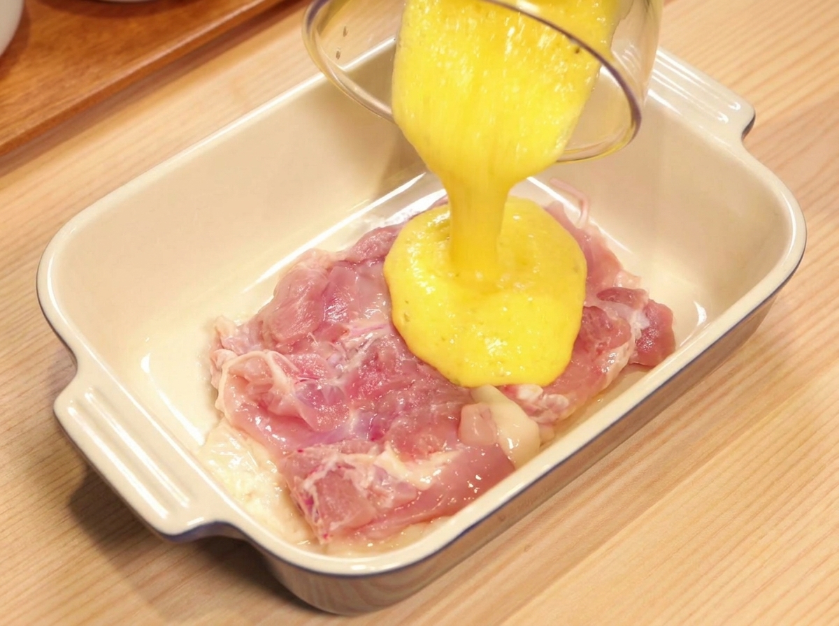 Gelber Ananassaft wird über eine rohe Hähnchenkeule in einer Keramikschale gegossen.