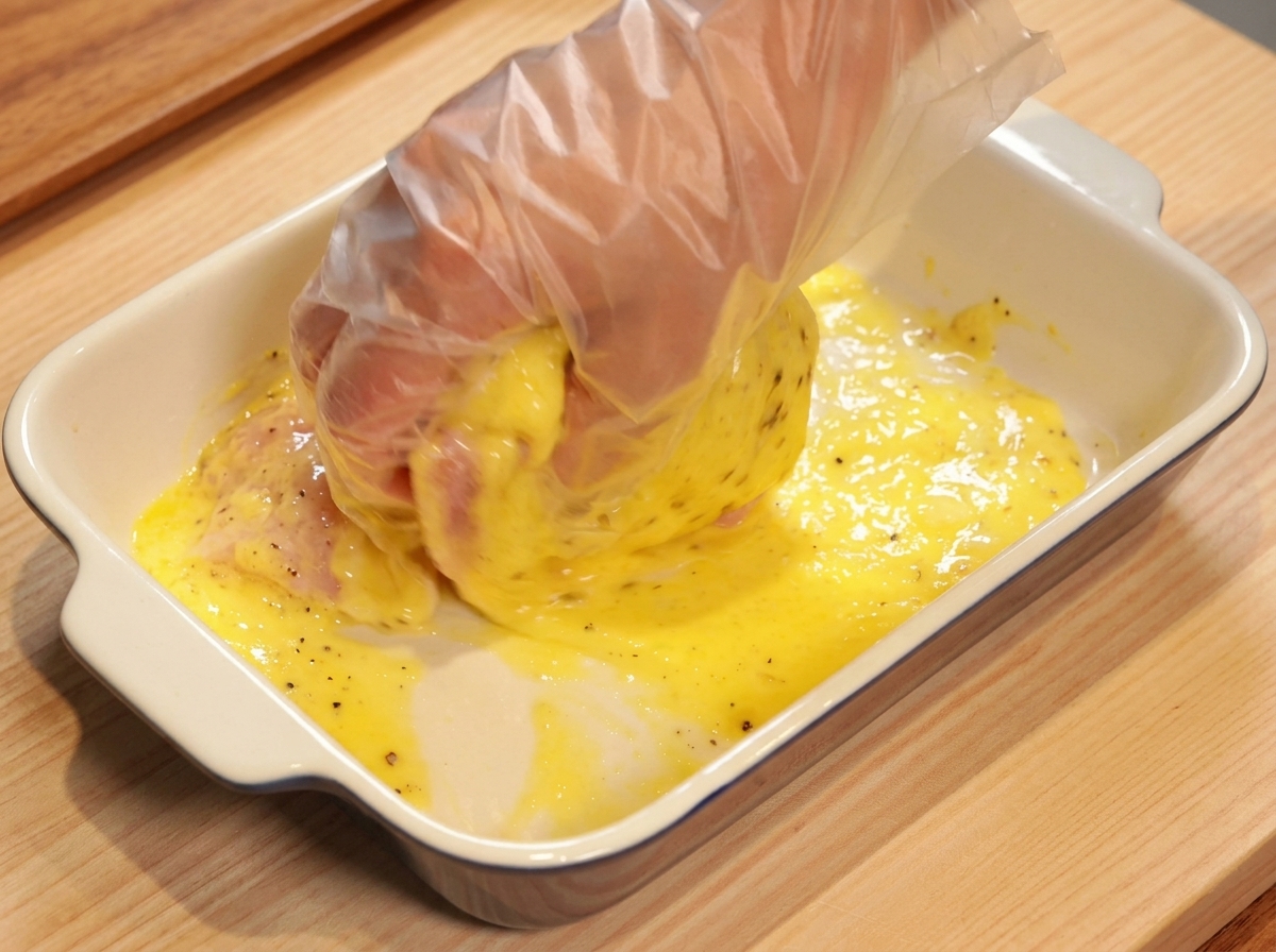 Eine Hand mit Handschuh massiert die Ananas-Marinade in das rohe Hähnchenfleisch ein.