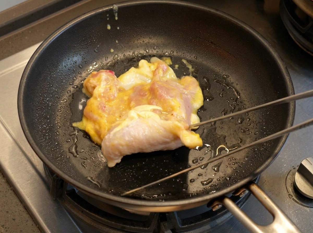 Eine Hähnchenkeule wird mit einer Zange in eine heiße, geölte Pfanne gelegt.