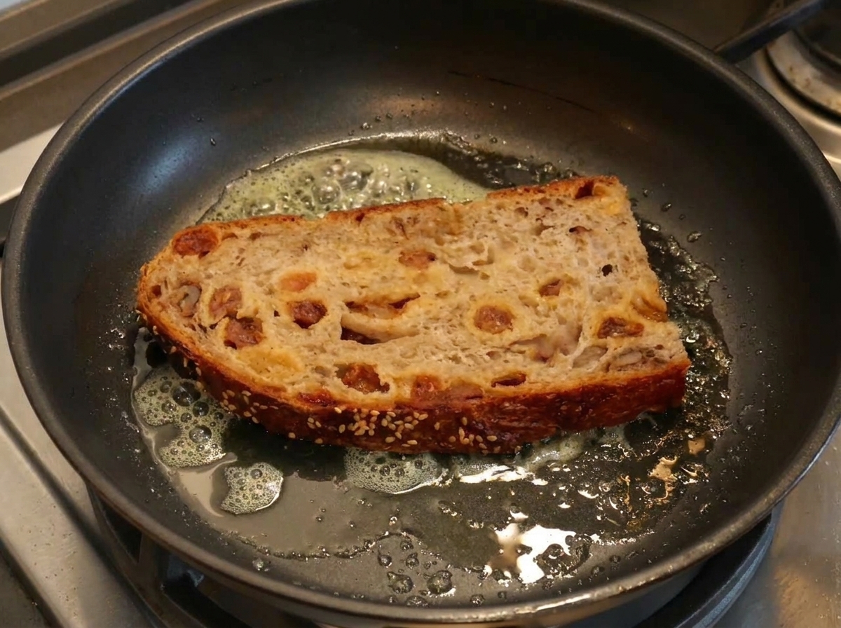 Eine dicke Scheibe Brot wird in einer Pfanne mit schäumender Butter geröstet.