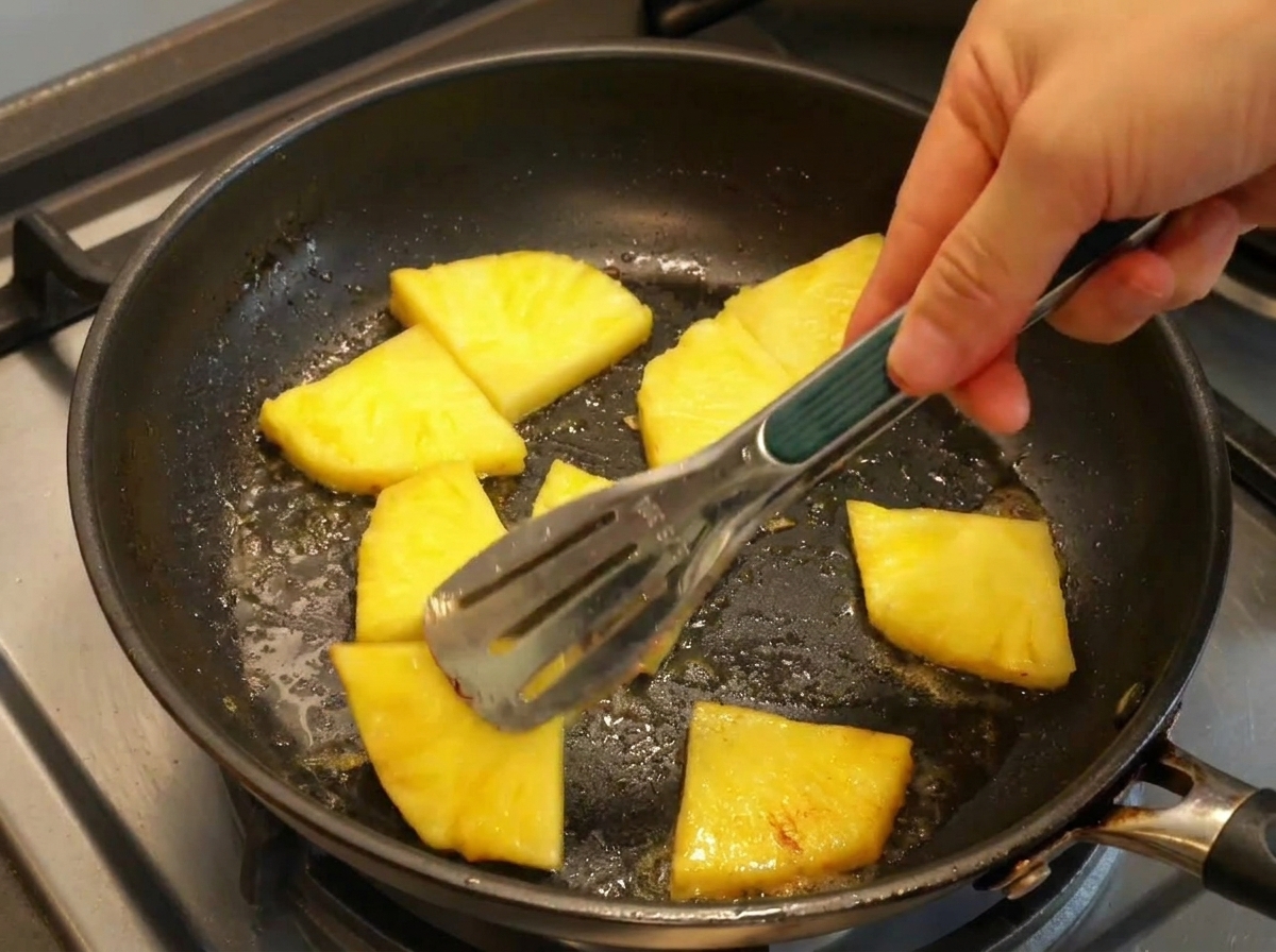 Ananasscheiben werden in einer Pfanne mit Butter gewendet und karamellisiert.