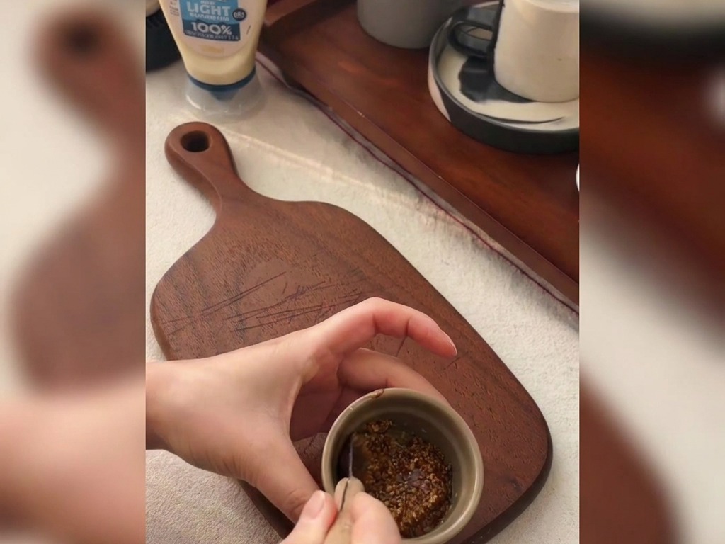 Hände mischen groben Senf und Honig mit einem kleinen Löffel in einer Keramikschale.