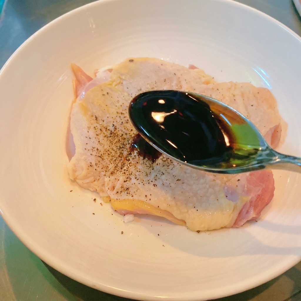 Ein Metalllöffel gießt dunkle Sojasauce über ein Stück Hähnchenfleisch.