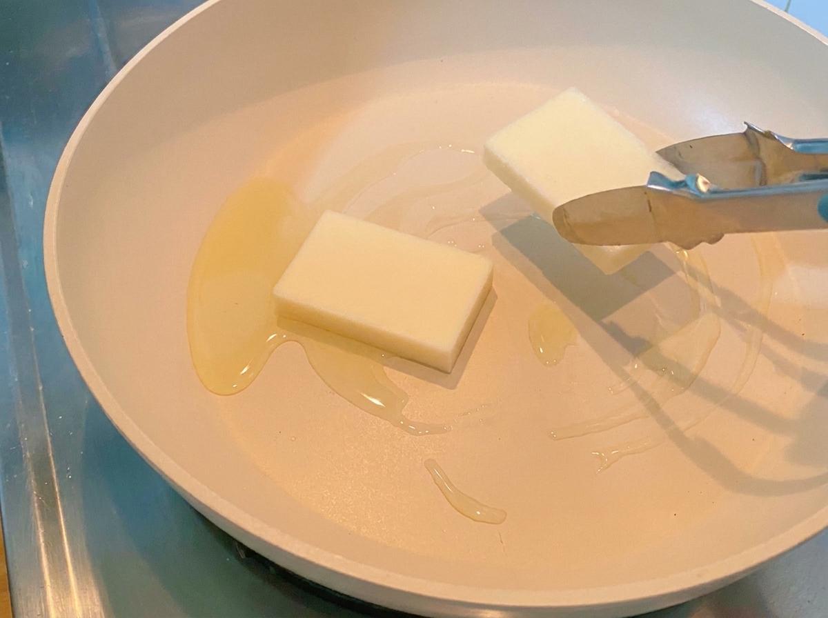 Eine Zange legt zwei dicke, weiße Reiskuchen in die heiße Pfanne.