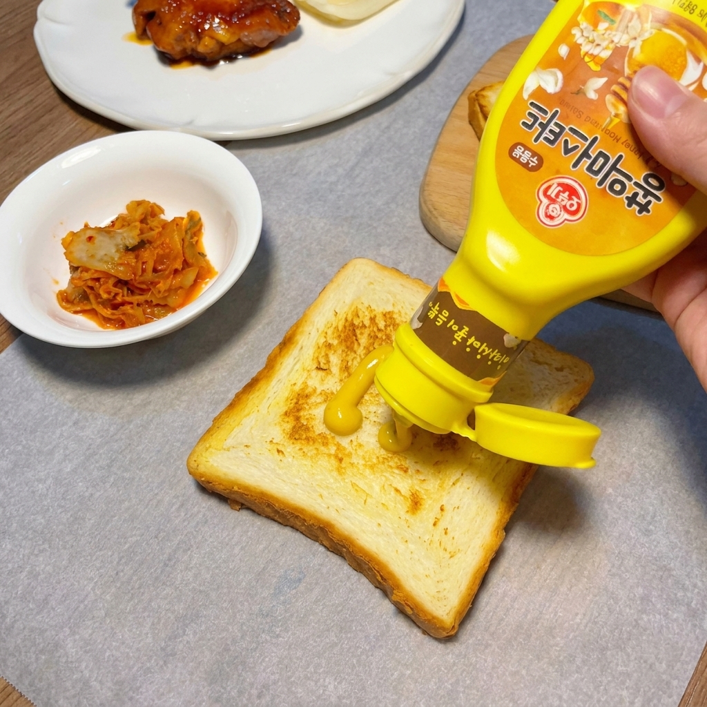 Gelber Senf wird in einem Zickzack-Muster auf den gerösteten Toast gestrichen.