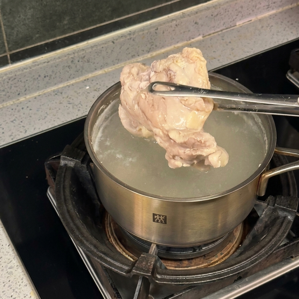 Ein Stück Hähnchen wird mit einer Metallzange über einem Edelstahltopf mit kochendem Wasser gehalten.